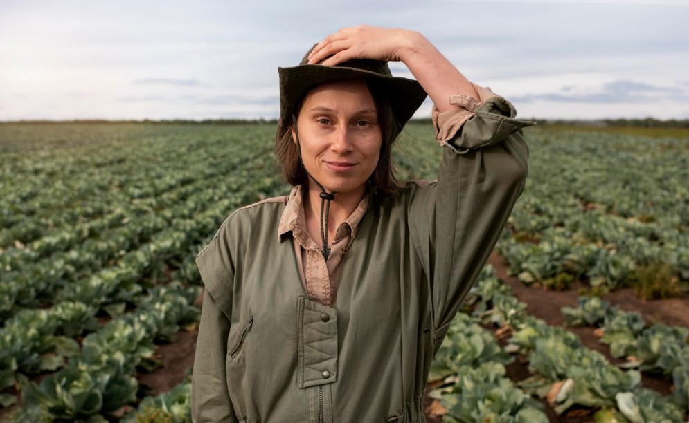 a successful female farmer standing and smiling while touching her hat in a field