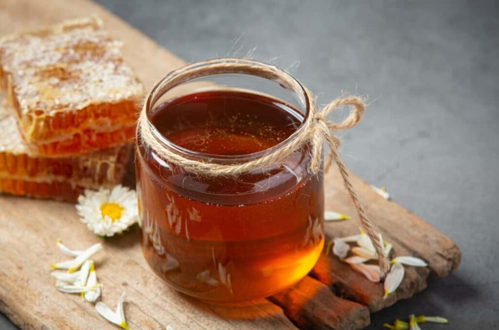 Honey jar with twine, next to honeycomb on a wooden surface