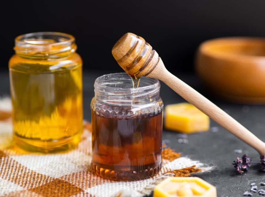 Glass jars of honey with a dipper, surrounded by lavender